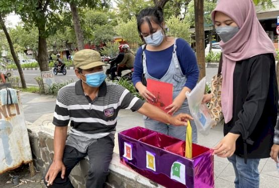 Dua mahasiswi Unair sedang menyaksikan warga belajar memilah sampah/Ist