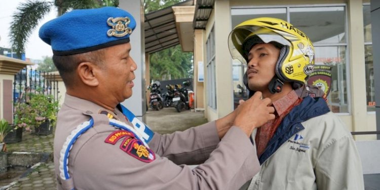 Salah satu anggota Propam Polri saat bantu masyarakat memasangkan helm/Ist